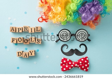 Jovial April Fool's setup: top view of wood letters spell 'April Fool Day', paired with a clown wig, mustache, bow tie, and eyeglasses, on a pastel blue background with scattered confetti Royalty-Free Stock Photo #2436661819