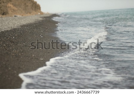 Lake waves with foam on the shore with volcanic sand