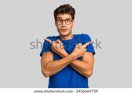 Young caucasian handsome man isolated points sideways, is trying to choose between two options. Royalty-Free Stock Photo #2436669739