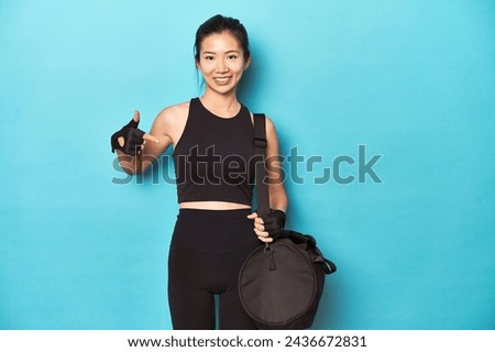 Asian woman with gym gear, ready for workout session, person pointing by hand to a shirt copy space, proud and confident