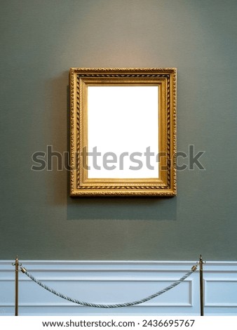 Mockup vertical white blank space in classic gold wooden square frame hanging isolated on luxury blue background behind display stanchions. Empty single vintage golden rectangular frame in museum.