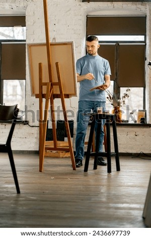 general shot young artist in a blue t-shirt in an art studio working on a painting