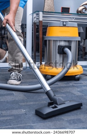 Anonymous shot of a man in casual wear using a vacuum cleaner with a brush nozzle attachment to clean the office carpet.
