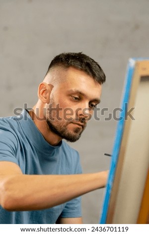 young artist in a blue t-shirt in an art studio working on a painting while sitting