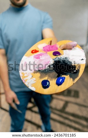 close up in an art studio an artist stands directly at the camera and show a palette and
