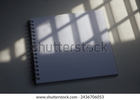 The blank cover page of the thick square textbook under the stripe pattern shadow from daylight for modern arts sketch idea, artwork design presentation, or architecture publishing branding mockup.