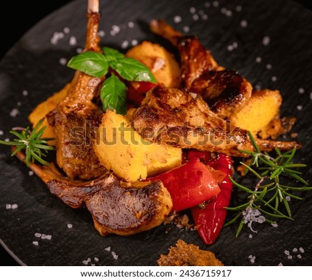 On a black porcelain plate, rack of lamb with fried polenta and hot peppers. Restaurant menu. Homemade food. Very beautiful and appetizing. Royalty-Free Stock Photo #2436715917
