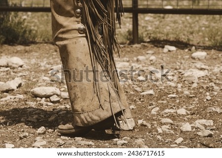 Cowboy walking on rocky ground in leather chaps, western wear in ranch lifestyle. Royalty-Free Stock Photo #2436717615