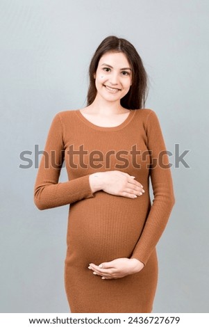 Happy pregnant woman touching her abdomen at Colored background. Future mother. Expecting of a baby. Copy space.