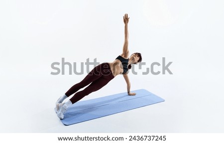 Young woman in sportswear, leggings and top standing on side plank position, training isolated over white studio background. Concept of sport, health and body care, fitness app, exercises templates