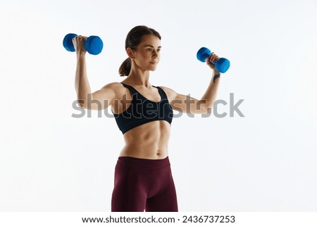 Young woman with sportive, muscular fit body in leggings and top training with dumbbells isolated over white studio background. Concept of sport, health and body care, fitness app, exercises templates