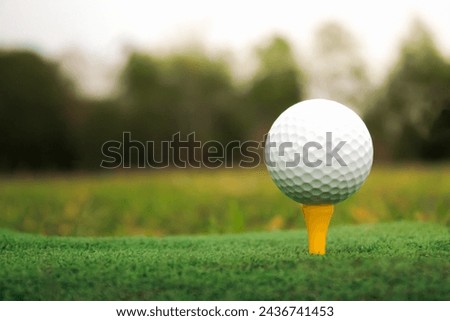 Take pictures in the evening Image of a golf ball set on a yellow tee. The background is blurry and has warm, soft lighting.