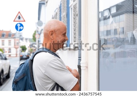 charismatic mature man, senior 60 years old stands by street window, reads real estate sales and rental advertisements, urban life, consumer behavior, and housing choices Royalty-Free Stock Photo #2436757545