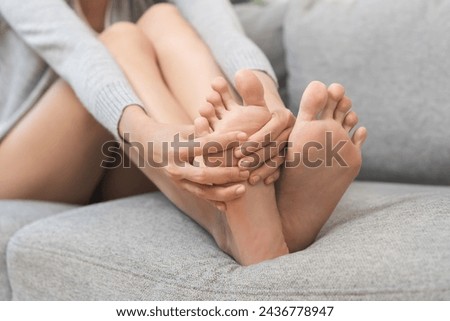 Foot pain concept, close up hand of young woman rubbing, massaging sore feet area of pain, girl suffering on sofa, couch at home. Discomfort painful feet ache from walking for long. Physical injury. Royalty-Free Stock Photo #2436778947