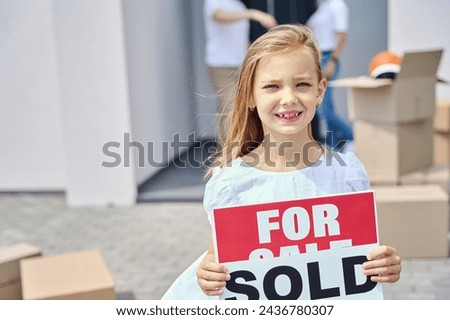 Cute girl stands in yard with signs for sale, sold