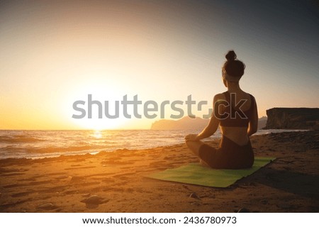 Yoga woman meditating at serene sunset or sunrise on the beach. The girl relaxes in the lotus position. Fingers folded in mudras.