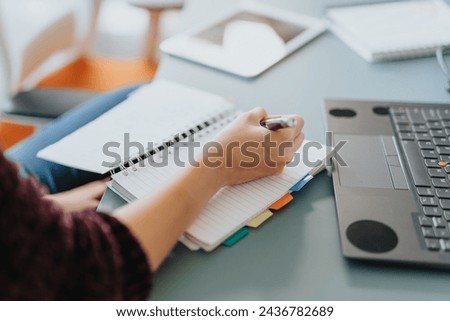 Businesswoman analyze statistics, plan for business growth, discuss projects, and strategize together in a cozy workplace. She is writing notes down in a notebook. Close up photo. Royalty-Free Stock Photo #2436782689