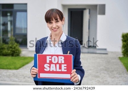 Young woman stands near country house with for sale sign