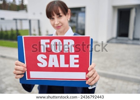 Female realtor stands with a for sale sign