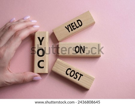 YOC - Yield on Cost. Wooden cubes with word YOC. Businessman hand. Beautiful pink background. Business and YOC concept. Copy space.