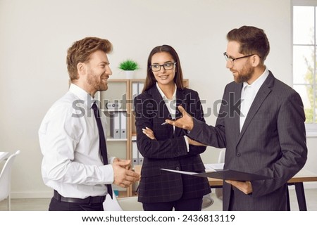 Portrait of three business people standing in office near the workplace discussing successful deal or signing contract. Coworkers talking with colleagues on a meeting considering new projects.
