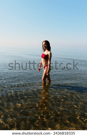 Young bikini model at the beach in red swimsuit. Summer holiday at the seaside where you can swim and play in the heat. Ready western european woman walking relaxing during a travel vacation