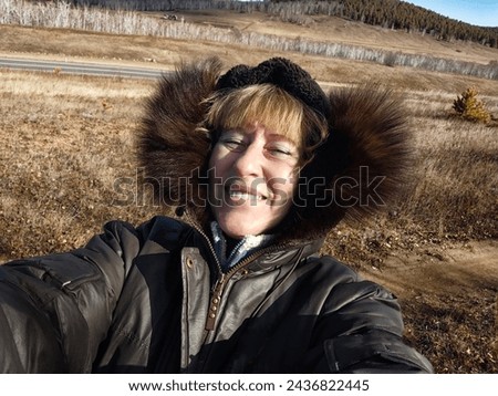 Happy female blonde tourist in a warm jacket taking selfie with outside in cold summer, autumn or winter day. Middle aged woman having fun in nature trip