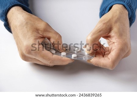 A person is holding a blister of pills and is taking one of them out. The pills are white and the blister is silver. Concept of taking medication and addition to pills. Royalty-Free Stock Photo #2436839265