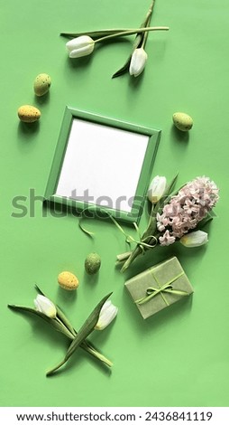 A picture frame with copy-space is placed next to a gift box and spring flowers, featuring white tulips and pink hyacinth in full bloom.