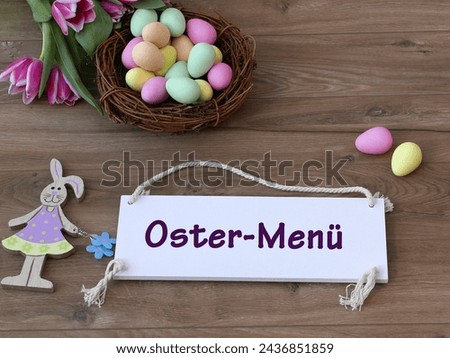 The text Easter menu written on a sign with Easter decorations and flowers. German inscription translates as Easter menu.