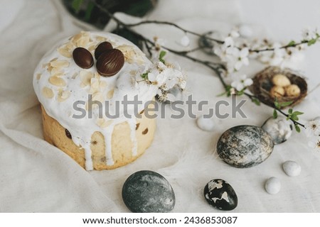 Happy Easter! Stylish easter eggs, homemade easter bread and spring flowers on linen napkin on rustic table. Natural painted marble eggs and cherry blooms, minimal still life