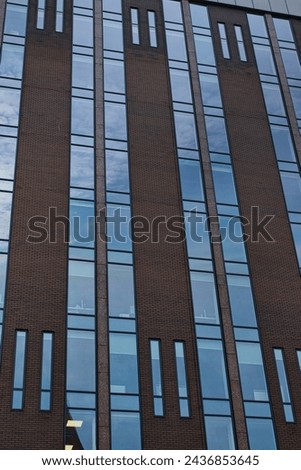 Modern building facade with a pattern of windows and brickwork against a blue sky in Leeds, UK.