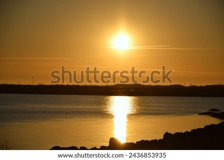 A serene view of the sun setting over a calm lake, casting a golden hue and reflection on the water Royalty-Free Stock Photo #2436853935
