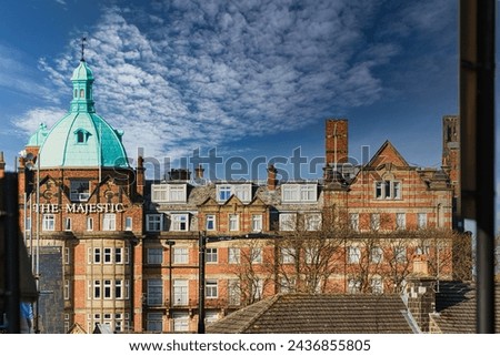 Vintage building with a green dome under a blue sky with fluffy clouds, viewed from a window in Harrogate, England.