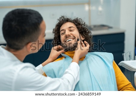 Smiling man at dentist appointment. Happy man with curly hair during teeth check-up at dental clinic.