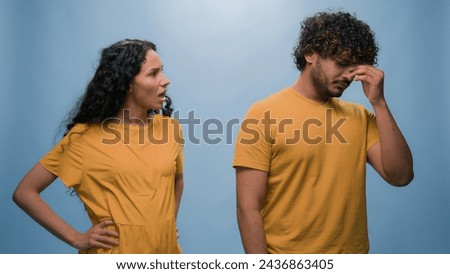 Sad tired Indian man cover ears offended ignore Arabian angry mad aggressive woman screaming shouting abuse jealous girl married couple quarrel problem divorce break up at blue studio background Royalty-Free Stock Photo #2436863405