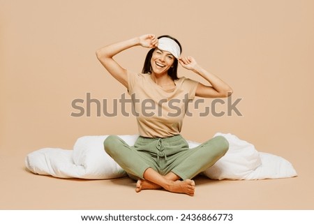 Full body young smiling calm Latin woman wears pyjamas jam take off sleep eye mask rest relax at home sitting with pillow duvet isolated on plain pastel beige background. Good mood night nap concept Royalty-Free Stock Photo #2436866773