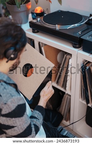 Audiophile with headphones selects a vinyl record from a shelf to play on a turntable. Royalty-Free Stock Photo #2436873193