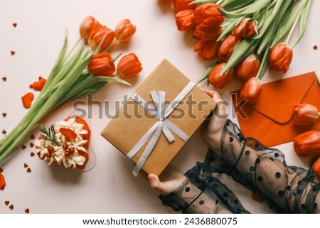 Gift box with a bow and tulips in the hands of a girl, festive background.