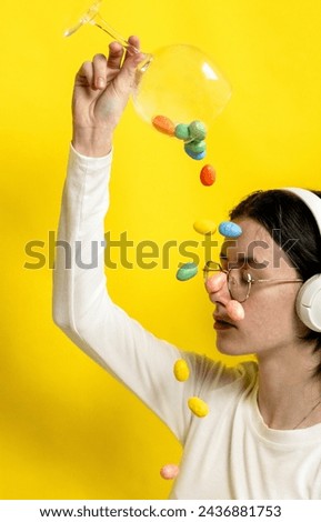 A teenage girl pours Easter eggs onto her face from a wine glass.