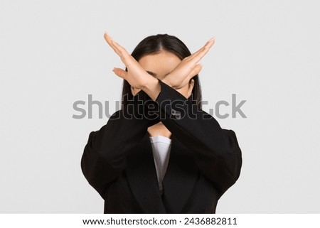Professional young businesswoman in black suit making timeout sign gesture with her hands over her face, standing against grey studio background