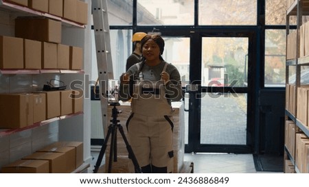 Warehouse manager using smartphone placed on tripod to make training video for interns. Supervisor filming herself in storage room showing trainees how to store merchandise, dolly out shot
