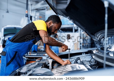 Specialist in car service uses torque wrench to tighten screws after replacing engine. African american adept auto repair shop employee uses professional tools to fix customer automobile Royalty-Free Stock Photo #2436886909