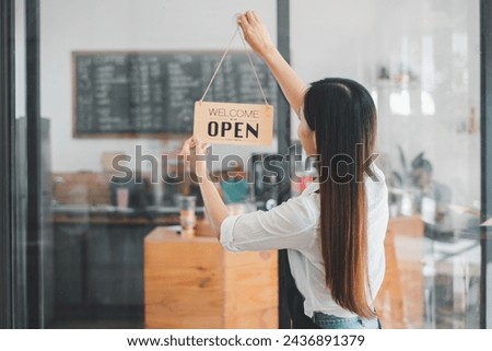 A dedicated cafe owner hangs an inviting 'Welcome Open sign, signaling the start of the day in her cozy coffee shop, an emblem of small business hospitality and readiness.