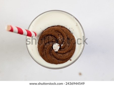 A refreshing vanilla milkshake with a chocolate dipped biscuit on the rim of a tall glass and a red and white striped straw.