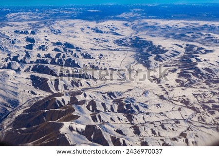 Capture the serene majesty of nature with this breathtaking aerial view showcasing the snow-dusted peaks of the Bayan Har Mountains, nestled on the border of Tibet and Qinghai. 