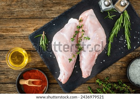 Raw rabbit thighs on cutting board with seasonings on wooden table 