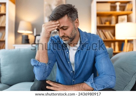 Closeup of man suffering from headache at home, touching his temples, copy space, blurred background. Migraine, headache, stress, tension problem, hangover concept
