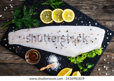 Fresh raw halibut fillet with lemon and dill on black stony cutting board on wooden table 