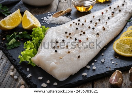Fresh raw halibut fillet with lemon and dill on black stony cutting board on wooden table 